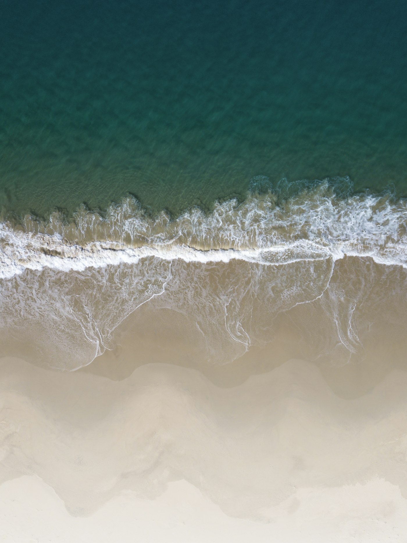 An aerial view of white surf meeting pale sand and dark turquoise water on Bruny Island.