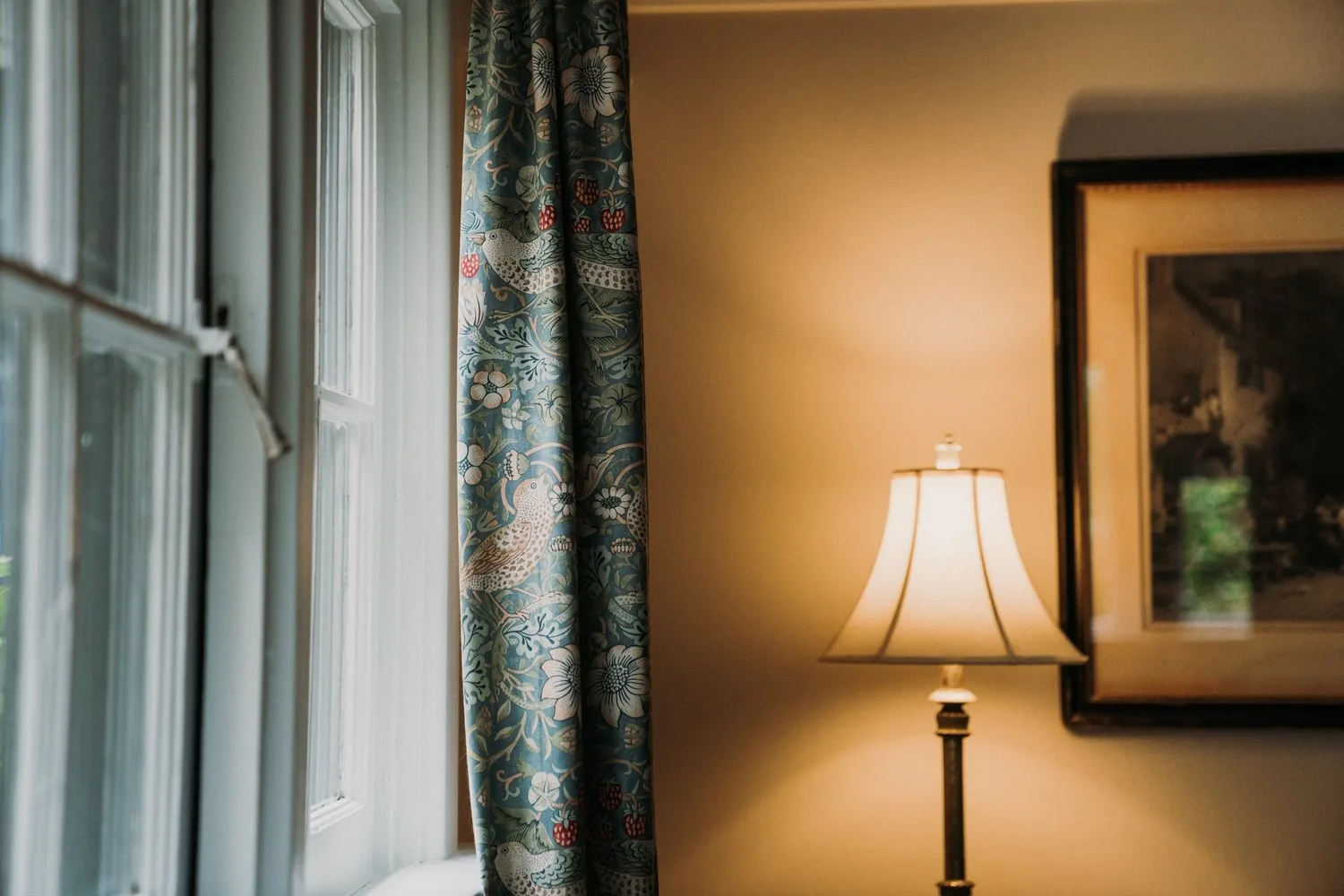 A glowing lamp beside patterned curtains.